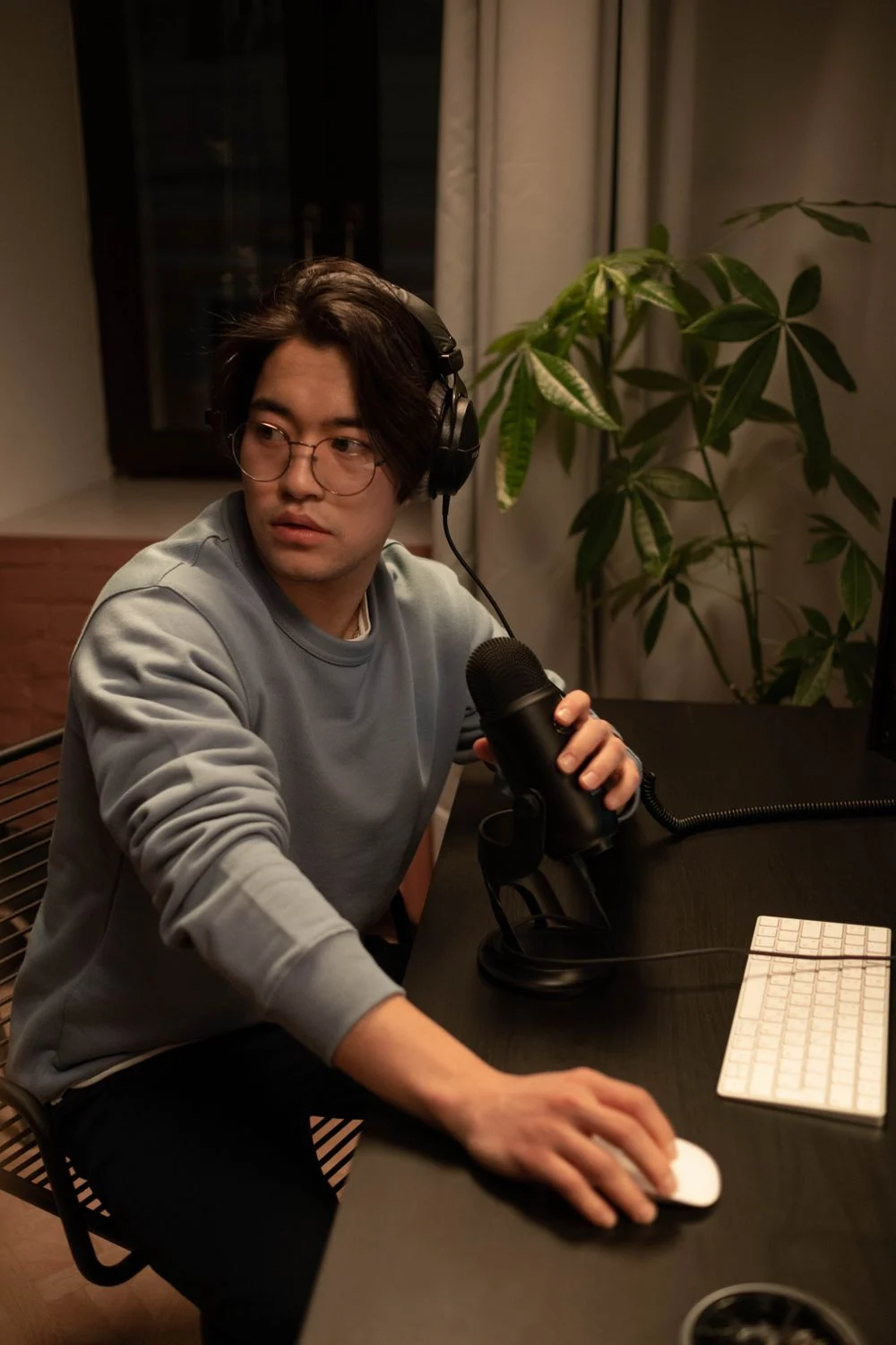 A person wearing headphones and holding a microphone at a recording desk.